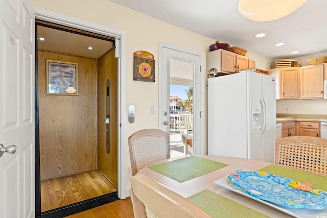 kitchen with light brown cabinets, light wood-type flooring, elevator, and white refrigerator with ice dispenser