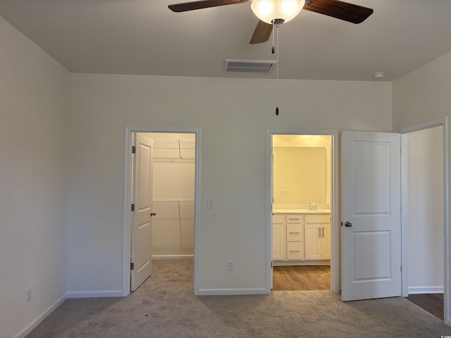 unfurnished bedroom with a walk in closet, sink, ceiling fan, light colored carpet, and a closet