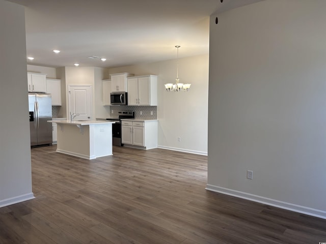 kitchen featuring white cabinetry, dark hardwood / wood-style flooring, decorative light fixtures, a center island with sink, and appliances with stainless steel finishes