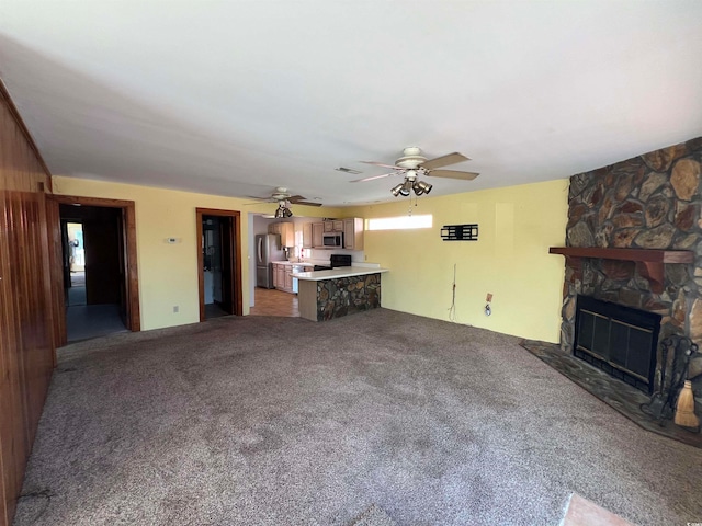 unfurnished living room featuring a fireplace, light colored carpet, wooden walls, and ceiling fan