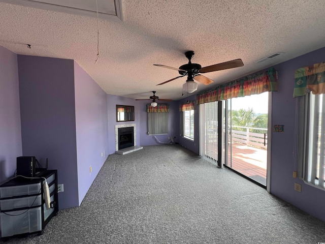 unfurnished living room featuring a tiled fireplace, a textured ceiling, carpet flooring, and ceiling fan