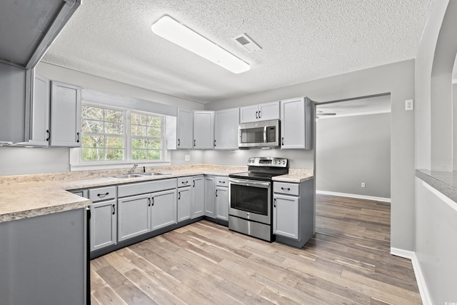 kitchen with stainless steel appliances, light hardwood / wood-style floors, gray cabinetry, and sink