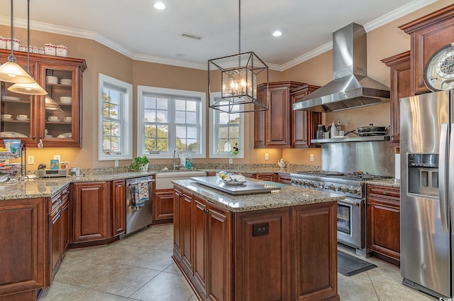 kitchen featuring stainless steel appliances, crown molding, wall chimney range hood, a kitchen island, and hanging light fixtures