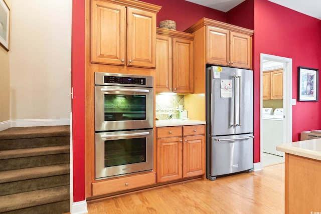 kitchen featuring light wood-type flooring, appliances with stainless steel finishes, backsplash, and washer and dryer