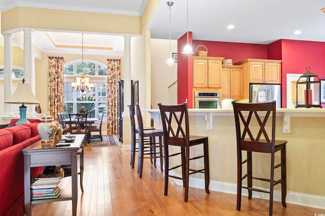 kitchen with stainless steel appliances, decorative light fixtures, light brown cabinets, an inviting chandelier, and light hardwood / wood-style floors