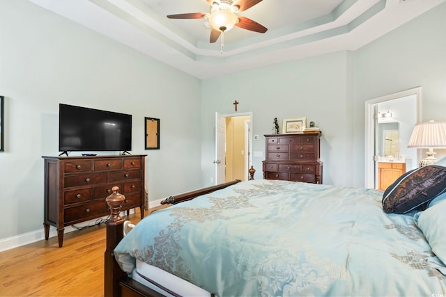 bedroom featuring light wood-type flooring, a tray ceiling, ceiling fan, and ensuite bathroom