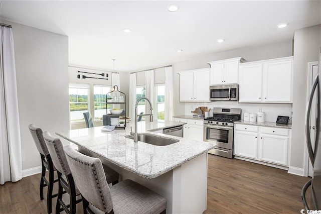 kitchen with sink, appliances with stainless steel finishes, an island with sink, light stone countertops, and white cabinets