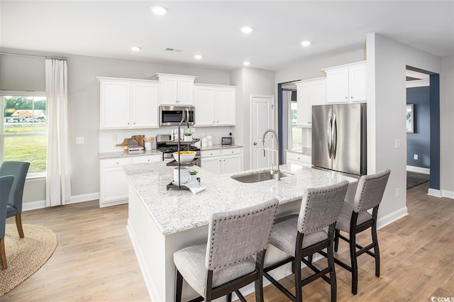 kitchen with sink, white cabinets, stainless steel appliances, light stone countertops, and a center island with sink