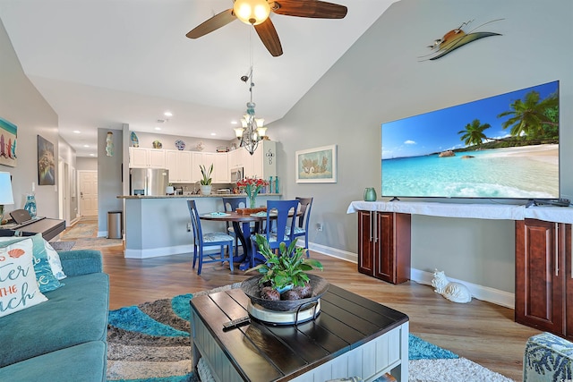 living room with light wood-type flooring, ceiling fan with notable chandelier, and high vaulted ceiling