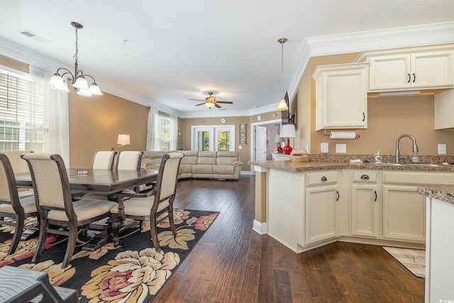 kitchen with light stone counters, crown molding, hanging light fixtures, sink, and dark wood-type flooring