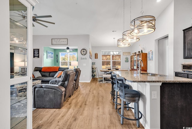 interior space featuring sink, light stone counters, a breakfast bar area, hanging light fixtures, and light wood-type flooring