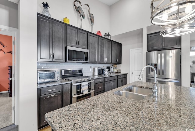 kitchen featuring stainless steel appliances, light stone countertops, sink, and a kitchen island with sink