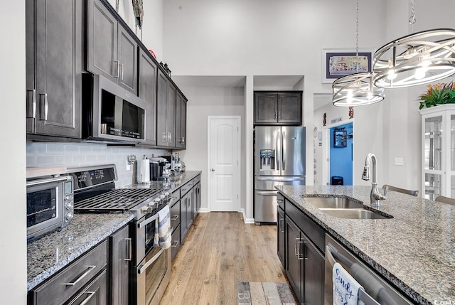 kitchen with light hardwood / wood-style floors, stainless steel appliances, sink, dark brown cabinets, and dark stone countertops