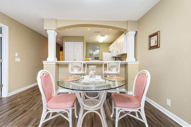 dining area featuring dark wood-type flooring and decorative columns