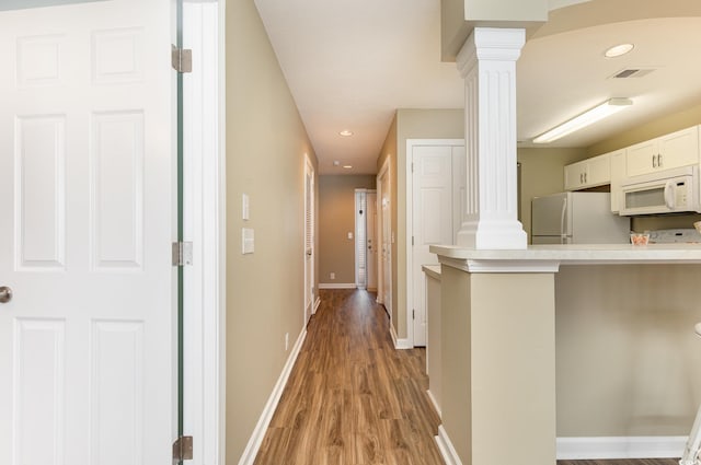 corridor with hardwood / wood-style floors and ornate columns