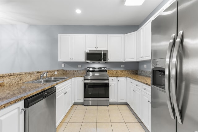 kitchen featuring stainless steel appliances, dark stone counters, light tile patterned floors, sink, and white cabinets