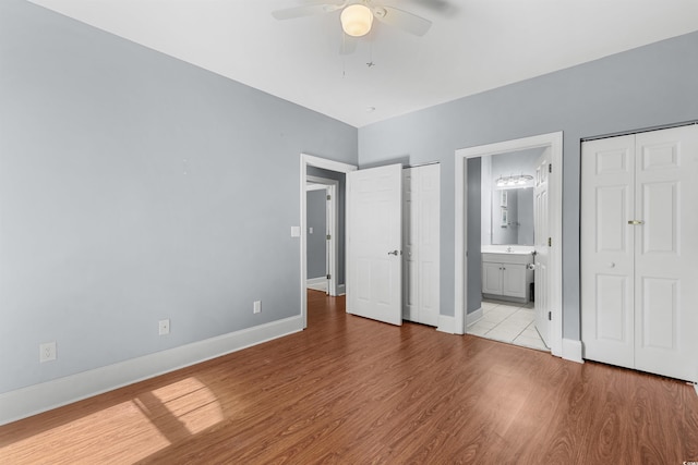 unfurnished bedroom with light wood-type flooring, sink, two closets, ceiling fan, and ensuite bathroom