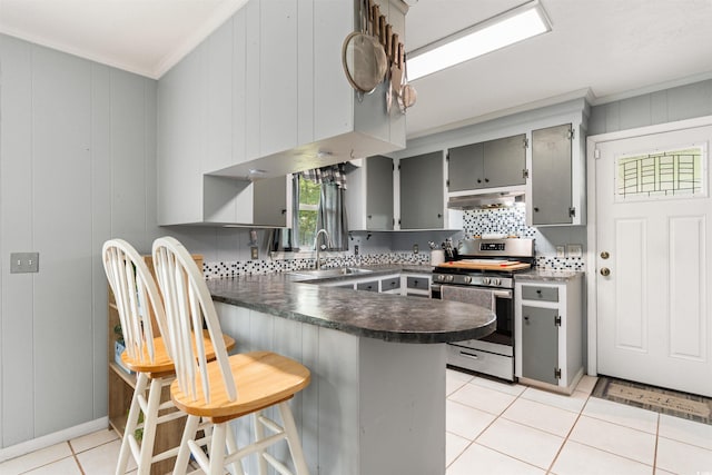 kitchen featuring kitchen peninsula, light tile patterned floors, gray cabinetry, stainless steel stove, and backsplash