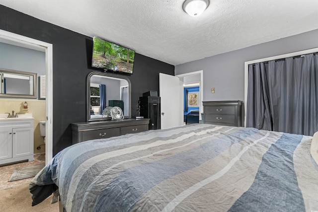 carpeted bedroom with connected bathroom, sink, a textured ceiling, and tile walls