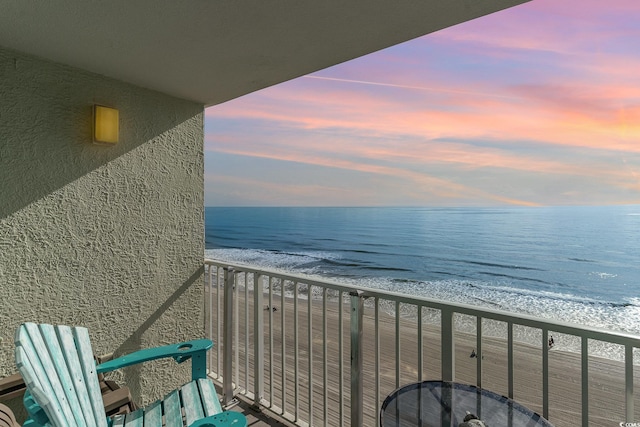 balcony at dusk featuring a view of the beach and a water view