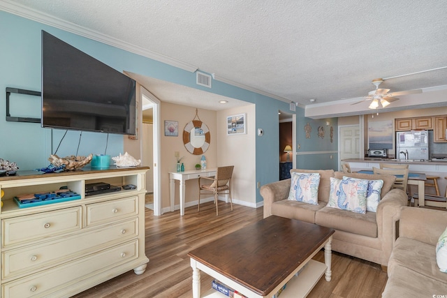 living room featuring ornamental molding, light wood-type flooring, a textured ceiling, and ceiling fan