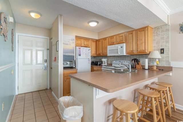 kitchen featuring kitchen peninsula, a kitchen bar, a textured ceiling, backsplash, and white appliances