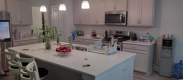 kitchen with appliances with stainless steel finishes, a center island with sink, light hardwood / wood-style flooring, and pendant lighting