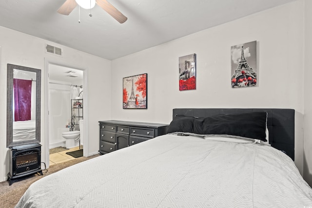 carpeted bedroom with ceiling fan, a wood stove, and ensuite bathroom