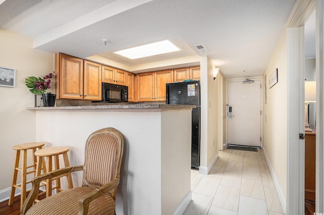 5308 N Ocean Blvd Unit 1014, Myrtle Beach, SC 29577 - kitchen featuring black appliances, baseboards, a peninsula, and a kitchen bar