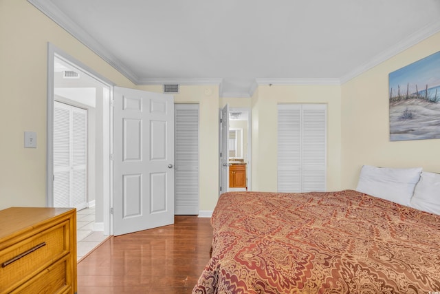 bedroom with two closets, connected bathroom, dark hardwood / wood-style flooring, and crown molding