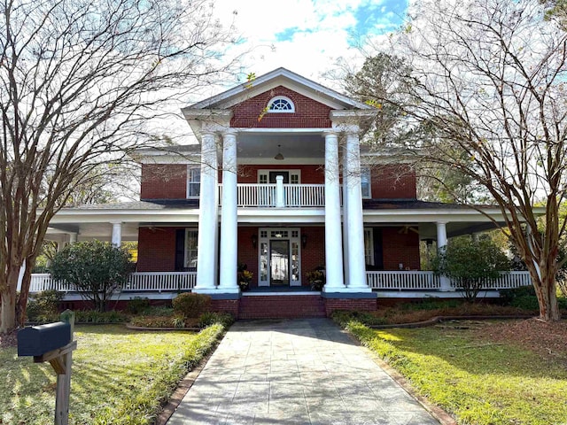 neoclassical / greek revival house with a porch, a front yard, brick siding, and a balcony