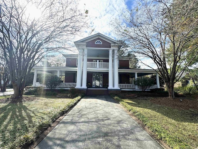 greek revival house with a front yard, covered porch, and a balcony