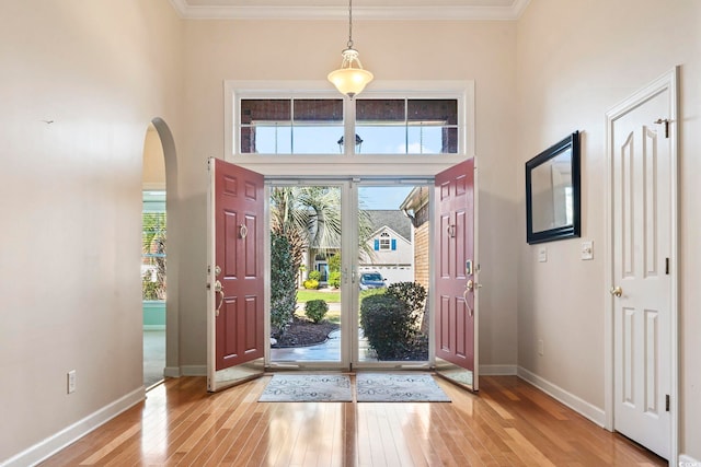 entrance foyer featuring a high ceiling, light wood-type flooring, ornamental molding, and plenty of natural light