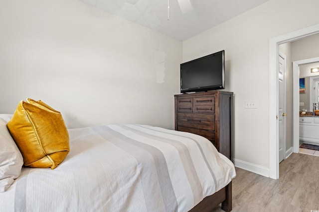 bedroom featuring light wood finished floors, ensuite bath, a ceiling fan, and baseboards