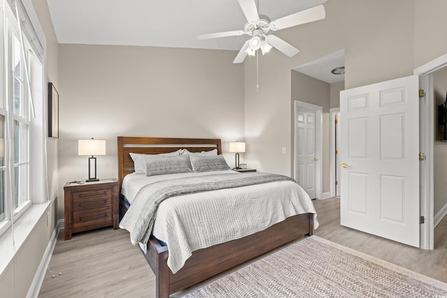 bedroom featuring a ceiling fan, a towering ceiling, light wood-style flooring, and baseboards