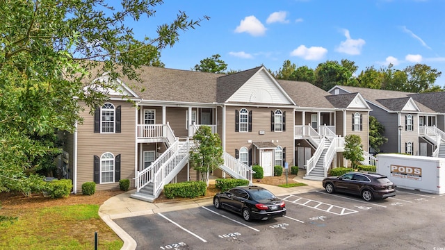 view of front of house featuring covered porch, uncovered parking, stairway, and roof with shingles