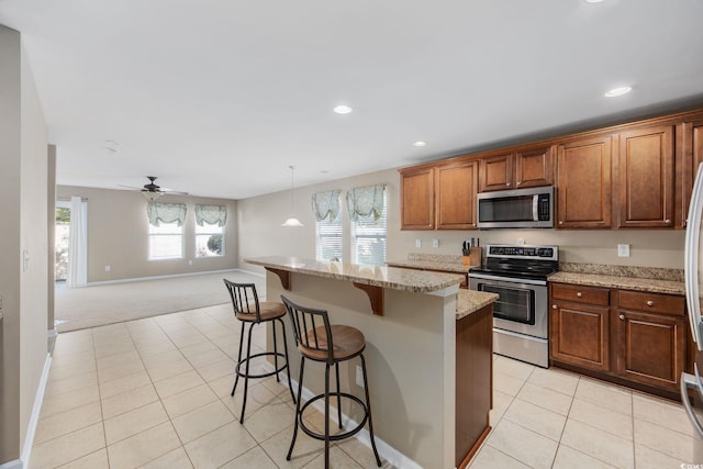 kitchen featuring light stone counters, decorative light fixtures, a kitchen breakfast bar, light colored carpet, and stainless steel appliances