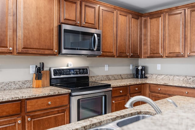 kitchen featuring stainless steel appliances, light stone countertops, and sink