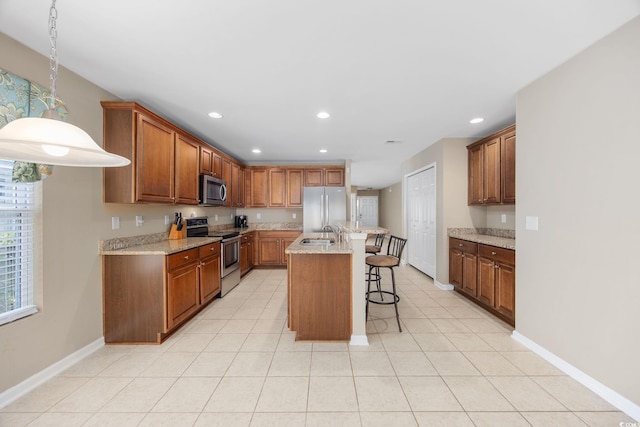 kitchen with a kitchen breakfast bar, hanging light fixtures, light stone counters, stainless steel appliances, and a center island with sink