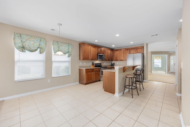 kitchen featuring appliances with stainless steel finishes, decorative light fixtures, a kitchen breakfast bar, a center island, and a healthy amount of sunlight