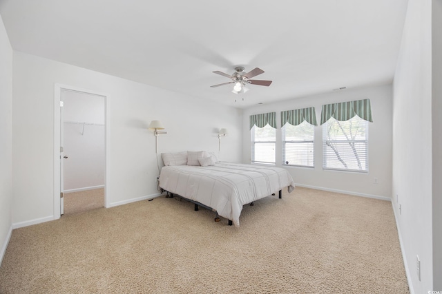 bedroom with a walk in closet, light colored carpet, ceiling fan, and a closet