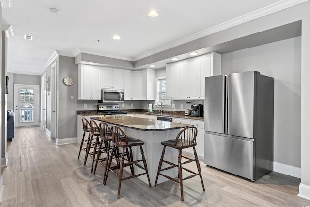 kitchen with a breakfast bar area, appliances with stainless steel finishes, light wood-style floors, ornamental molding, and white cabinets