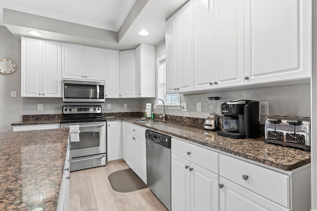 kitchen featuring crown molding, light wood-style flooring, appliances with stainless steel finishes, white cabinets, and a sink