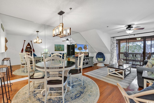 dining room featuring wood-type flooring, ceiling fan with notable chandelier, and a textured ceiling