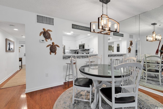 dining space with wood-type flooring, a notable chandelier, and a textured ceiling