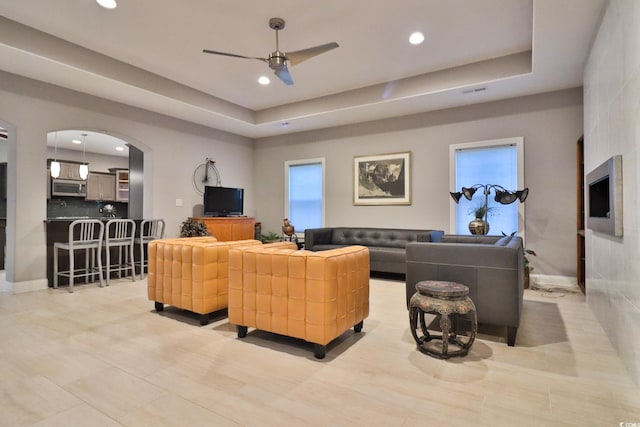 living room with a raised ceiling, plenty of natural light, and ceiling fan