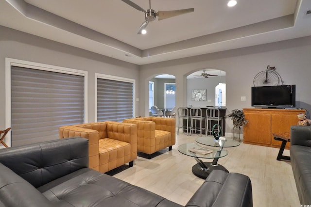 living room featuring a raised ceiling, ceiling fan, and light wood-type flooring