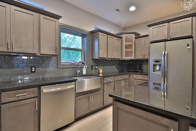 kitchen with sink, light hardwood / wood-style flooring, appliances with stainless steel finishes, tasteful backsplash, and dark stone counters