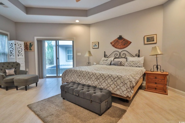 bedroom with wood-type flooring, a raised ceiling, and access to outside