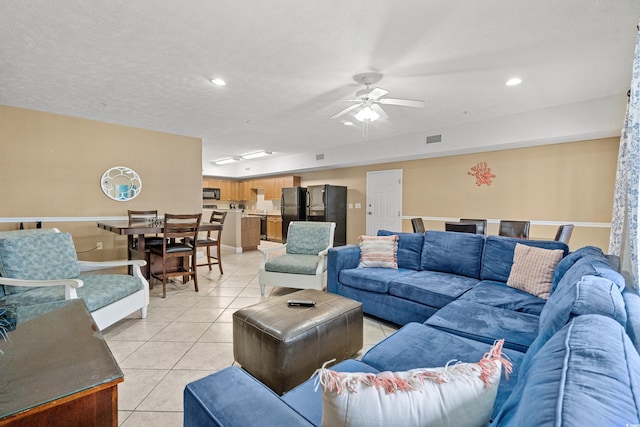 living room featuring a textured ceiling, light tile patterned floors, and ceiling fan